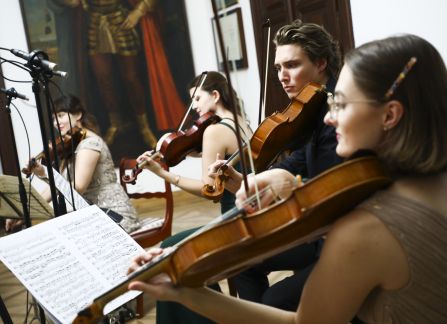A photograph. A string concert in Villa Decius. The musicians play the violin and the cello in the Ball Room at Villa Decius.